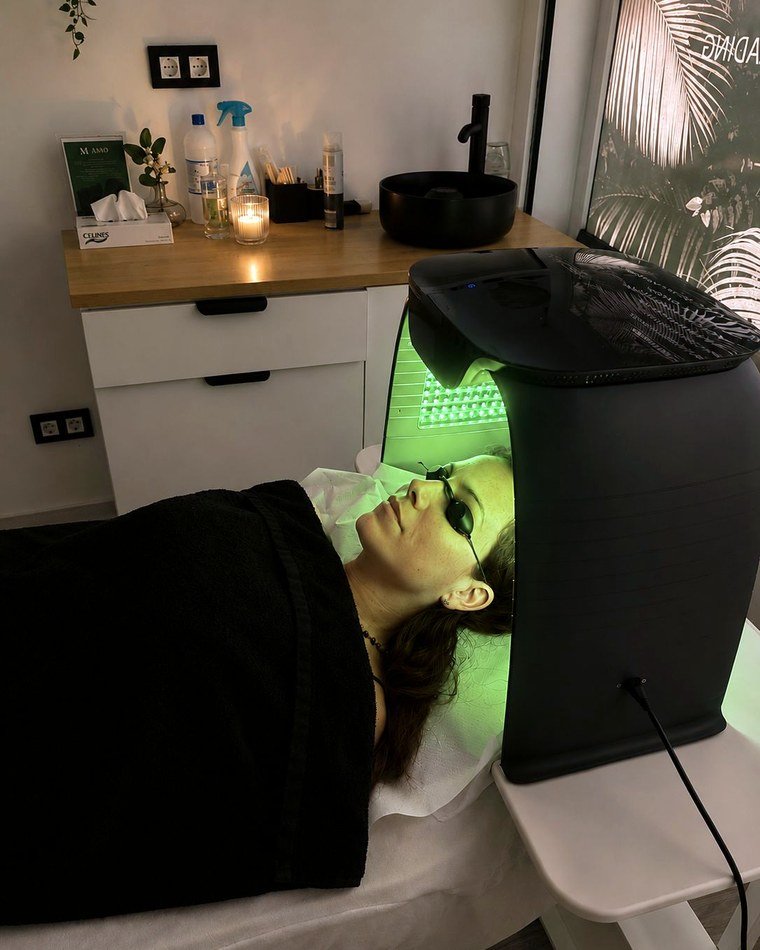 Paciente recibiendo un tratamiento facial con máscara de luz LED en la cabina de la clínica